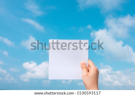 Woman hand holding white paper with blue sky and cloud background.