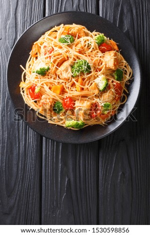 Spaghetti with broccoli, chicken, tomatoes, cheese and pumpkin close-up on a plate on the table. Vertical top view from above

