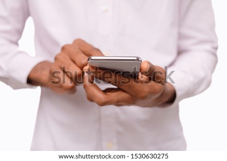 Unrecognizable black man using smartphone, browsing social media over white background, closeup