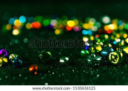 Colourful Christmas jingle bells. Dark green filter applied. Blurred bokeh glitter background. Shallow depth of field. For overlay, background or texture.