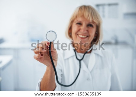 Holds stethoscope in hand. Portrait of senior doctor in white uniform that stands in the clinic.
