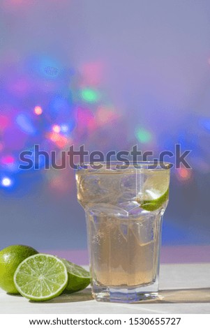 gin tonic accompanied with lemons on white table and colored lights background