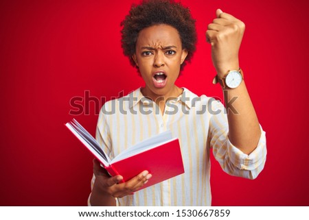 African american woman reading a book over red isolated background annoyed and frustrated shouting with anger, crazy and yelling with raised hand, anger concept
