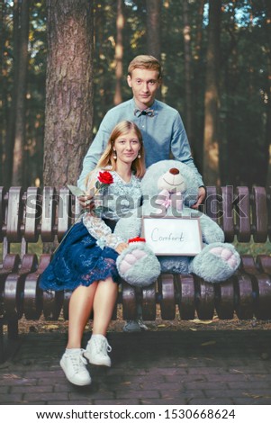 young guy gives a girl a red rose. couple together on a park bench. love and relationship concept