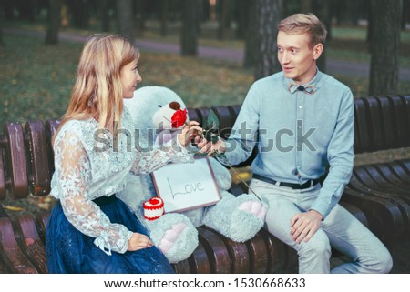 young guy gives a girl a red rose. couple together on a park bench. love and relationship concept