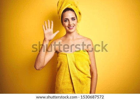 Beautiful woman wearing shower towel on body and head over yellow isolated background showing and pointing up with fingers number five while smiling confident and happy.