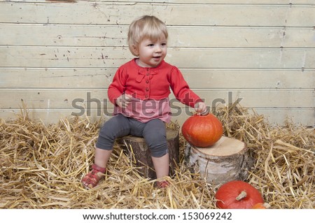 Little girl seated in a barn with straw and pumpkins