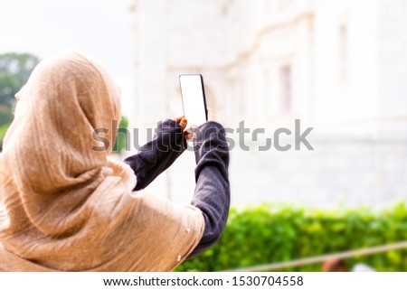 Young Burnett Muslim women wearing hijab and taking photos with smartphone