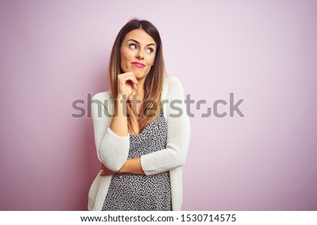 Young beautiful woman standing over pink isolated background looking confident at the camera smiling with crossed arms and hand raised on chin. Thinking positive.