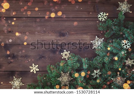 Rustic Natural Christmas background with border of fluffy green fir branches and wooden snowflakes on textured dark brown plank wood background. Copy space for text, flat lay, top view. Corner frame.