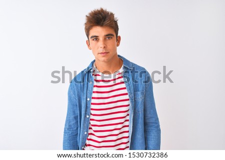 Young handsome man wearing striped t-shirt and denim shirt over isolated white background with serious expression on face. Simple and natural looking at the camera.