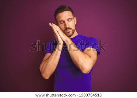 Young man wearing casual purple t-shirt over lilac isolated background sleeping tired dreaming and posing with hands together while smiling with closed eyes.