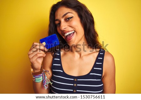 Young beautiful woman holding credit card standing over isolated yellow background with a happy face standing and smiling with a confident smile showing teeth