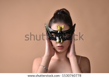 Beautiful young girl in a bat mask prepared for the celebration of Halloween. Studio photo. Woman on a beige background in a T-shirt and carnival glasses. Girl in a bat mask.
