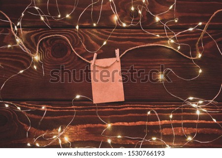 Clothespins with a blank sheet of paper hanging on a background of a background framed from a garland
