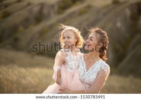 Mom with daughter in pink fairy-tale dresses walk in nature. Little princess childhood.