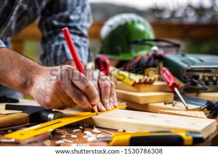 Adult carpenter craftsman with a pencil and the carpenter's square trace the cutting line on a wooden table. Construction industry, housework do it yourself. Stock photography.