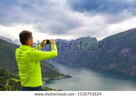 Slender man in a yellow jacket from a height photographs on the smartphone the most popular fjords in Norway