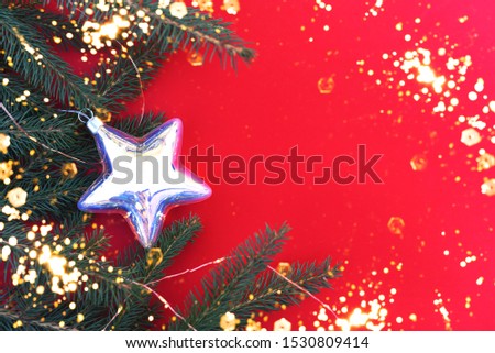 Christmas flat lay on a red background with a Christmas tree branch and a large holographic Christmas tree toy star.Glowing star.