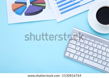Computer keyboard with diagrams and cup of coffee on blue background