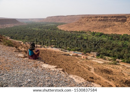 Girl explorer traveler girl watching a canyon and a oasis on top of a viewpoint in Morocco, Africa
