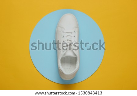 Stylish white sneaker on a yellow background with blue circle in the middle. Top view. Minimalism fashion still life