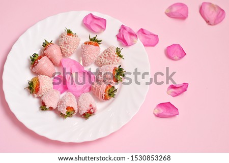 Glazed strawberries on the white plate with pink petals of rose flower beautiful flat lay composition top view on the pink background. Candy colors beautiful tasty yummy picture. Soft nice desert