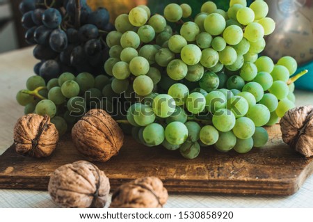 Autumn still life with grapes on a wooden board and walnuts around on a wooden white table. On the back scales. The concept of autumn harvest. Happy Thanksgiving. Selective focus. Template for design.