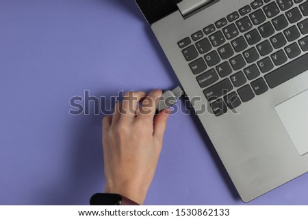 Female hand connects USB flash drive to laptop on purple paper background. Top view