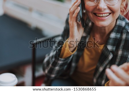 Cropped photo of a smiling woman in eyeglasses talking on the phone in a cafe