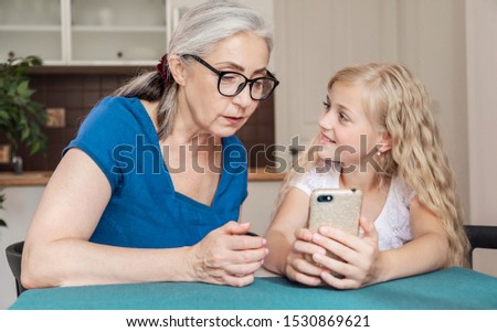 Preschool female kid teaching her grandmother some smartphone tips and tricks