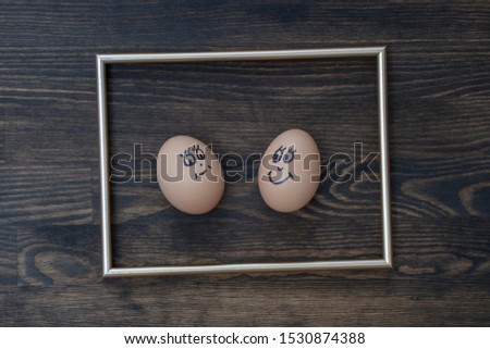 Picture golden frame and two funny eggs smiling on dark wooden wall background, close up. Eggs family emotion face portrait. Couple eggs with happy face for love concept