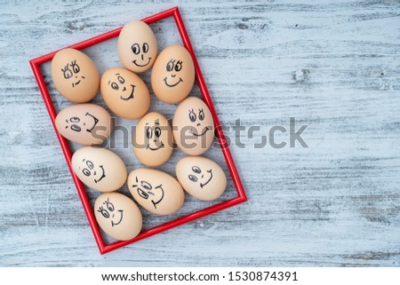 Picture red frame and many funny eggs smiling on white wooden wall background, close up. Eggs family emotion face portrait. Concept funny food. Copy space