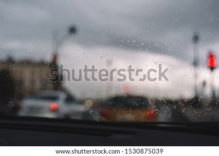 Close up photo of rain drops on windshield. Selective focus, blurred cars in traffic jam on background. Thin threads of glass heating. Rainy season. Automotive industry. Cosiness inside the car.