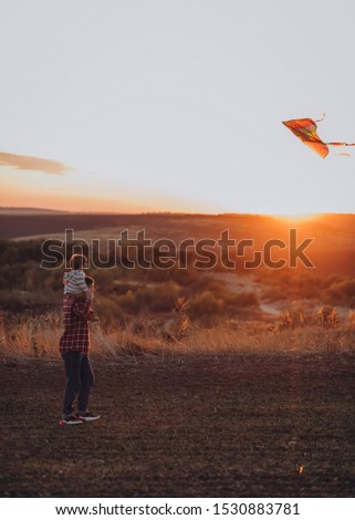 Mom dad and son launch a multi-colored kite into the air at sunset
