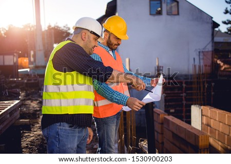 Men in hardhat and yellow and orange jacket posing on building site. stock photo