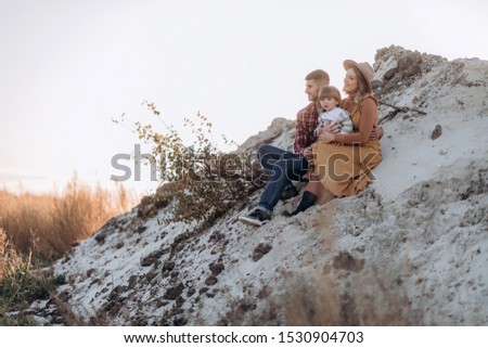 Young mother and dad playing, hugging, kissing with their little son in autumn field at sunset
