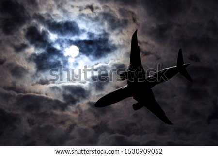 Full moon and silhouette passenger plane on  cloudy sky background. Danger of a airplane crash in bad weather. Dramatic Halloween night. Airliner makes a night flight in stormy weather. 