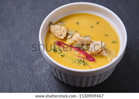 Pumpkin cream soup with breadcrumbs, hot pepper and thyme, garnished with pumpkin seeds.