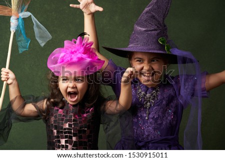 Cute child girl in witch costume for Halloween, close-up. Happy sisters on Halloween. Funny kids in carnival costumes on green background with copy space