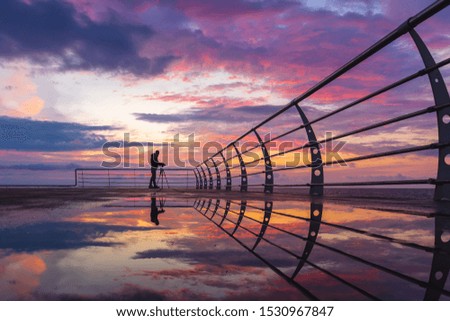 Silhouette of photographer on the pier with tripod beautiful  sunrise clouds background and reflections