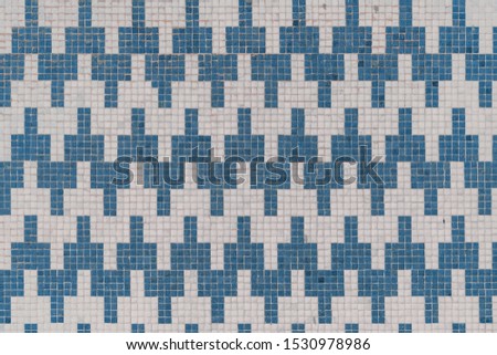 Front view of a tiled wall texture consisting of small stone mosaic tiles of white and blue color making a regular horizontal seamless pattern