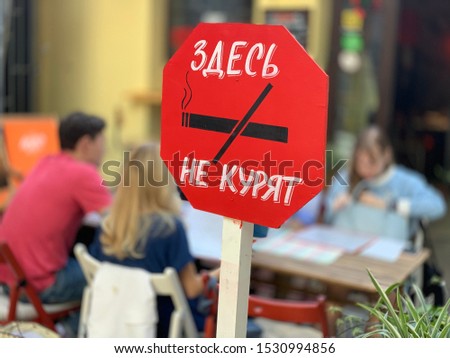 Red sign with writing in Russian “no smoking” people are sitting at the table on the background