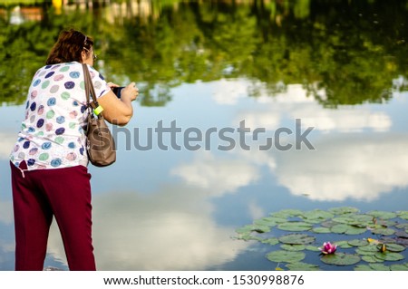 Mature woman takes pictures on a smartphone water Lily in the city pond