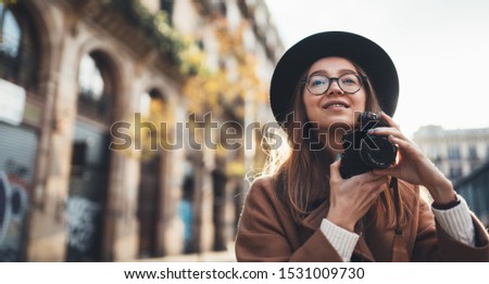 Photographer in glasses take photo on retro camera. Tourist portrait girl in hat travels in Barcelona holiday. Sunlight flare street in europe city. Traveler hipster shooting architecture, copy space