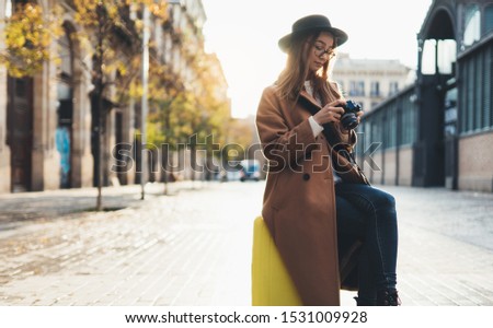 Photographer tourist with suitcase take photo on retro camera. Smiling girl in hat travels in Barcelona. Sunlight flare street in europe city. Traveler hipster shoot architecture, copy space mockup