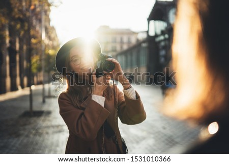 Photographer in glasses with retro camera take photo model girlfriend. Tourist smile girl in hat travels in Barcelona holiday with traveler friend. Sunlight flare street in europe. Photoshoot in city