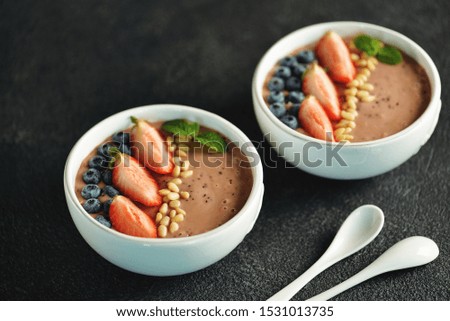 Smoothie bowl of strawberries and blueberries with pine nuts and mint.