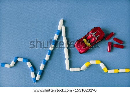 drawing a cardiogram from capsules on a blue background and a toy car with medical capsules, help concept.