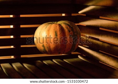 A bright orange pumpkin hangs in the air above a wooden surface against a background of walls made of wooden slats through which light breaks through. Mystical picture for the holiday Halloween